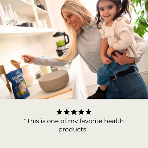 Woman holding a child in a kitchen with a Natura Fiber bag in the foreground. A 5-star review reading, "This is one of my favorite health products."